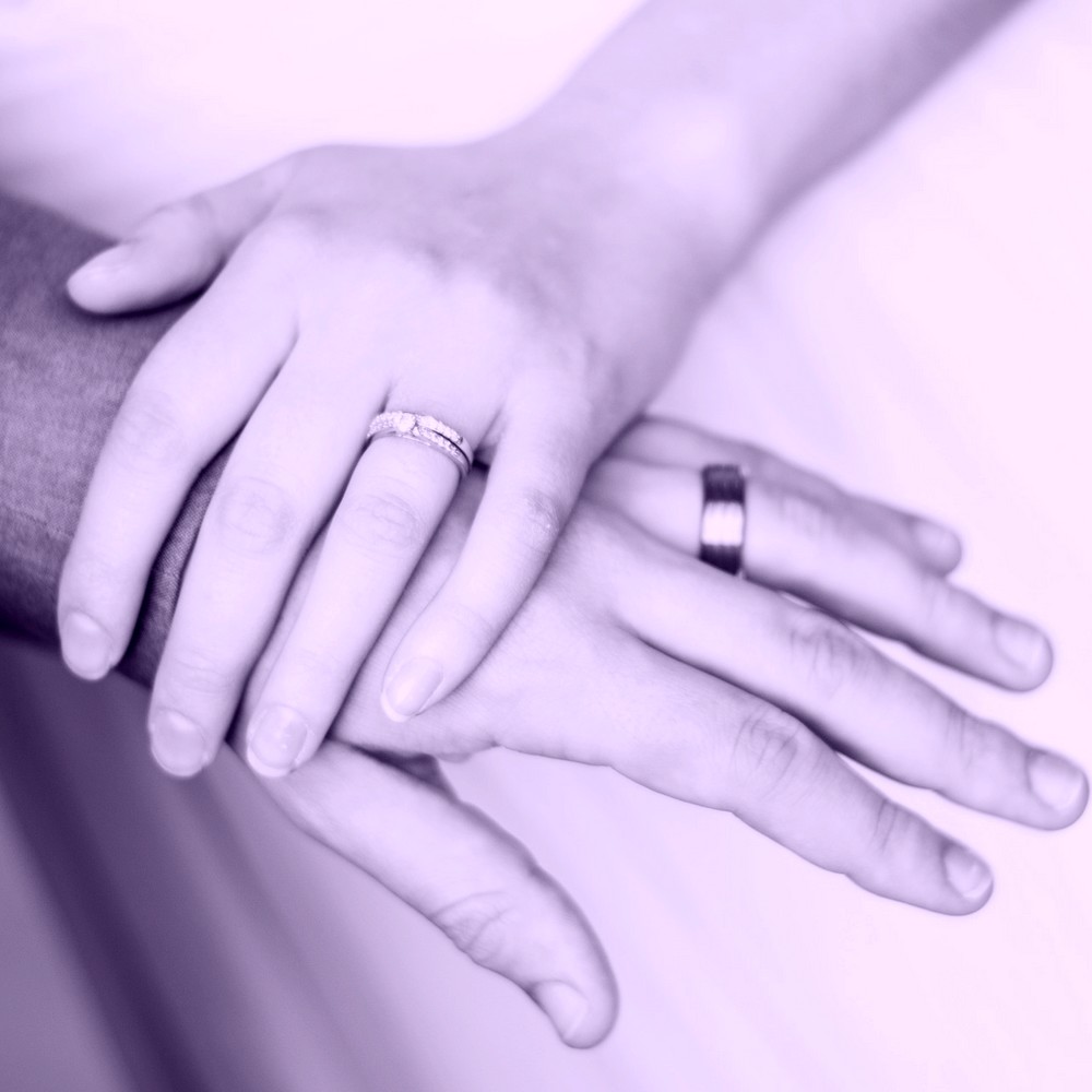 A woman's hand on a man's hand, both wearing wedding rings