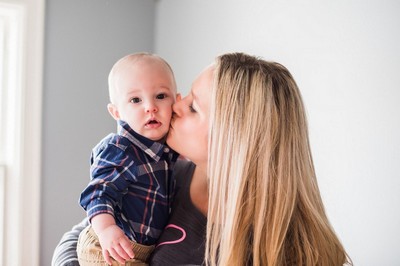A woman holding a baby and kissing it on the cheek.