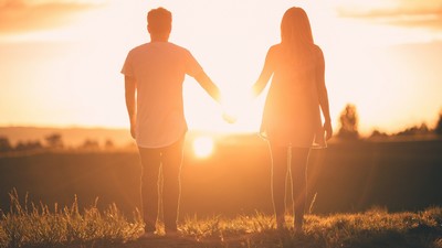 Man and woman holding hands and staring into the sunset.