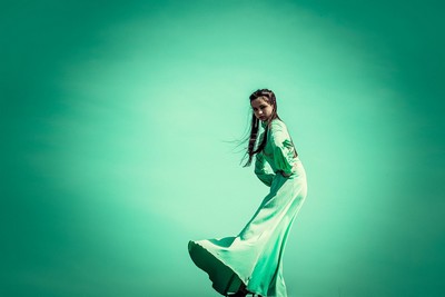 A person wearing a flowing white dress and dancing on a green background.