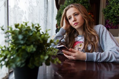 A woman sitting at a table looking at the phone and is sad.