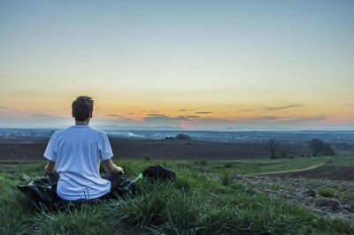 A person sitting on a grassy hill, overlooking a vast landscape during sunset.