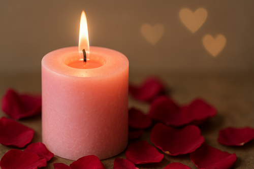 Pink pillar candle burning amid red rose petals with heart-shaped bokeh in the background—romantic love spell scene.