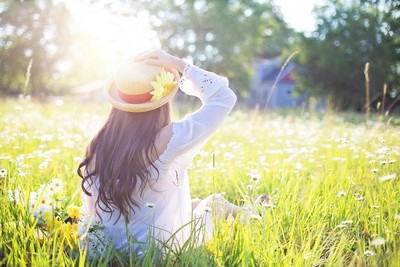 Girl in a straw hat sat in a field of flowers.