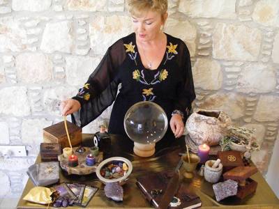 A photo of a person sitting at a table with various objects related to fortune telling and witchcraft.