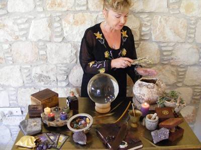 A woman poised over an Altar, wafting herbs.