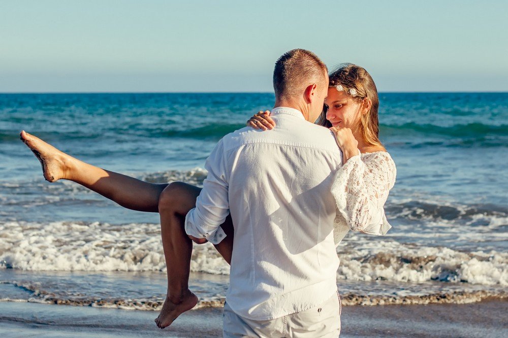 A happy couple embracing on the beach in the sunshine.