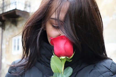 A young girl holding and smelling a red rose