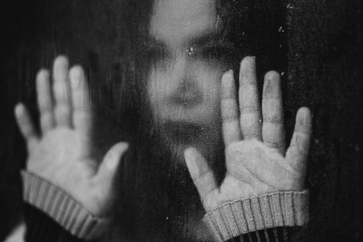 A woman inside with hands pressed against the window looking out at the rain.