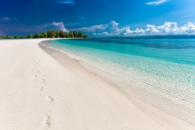 A serene beach with clear turquoise waters, white sands, and a blue sky with fluffy clouds.