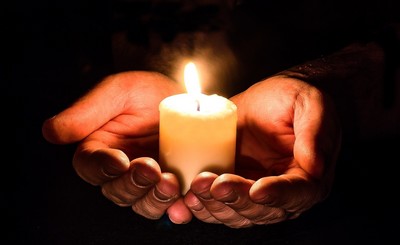 Two hands holding a white candle.